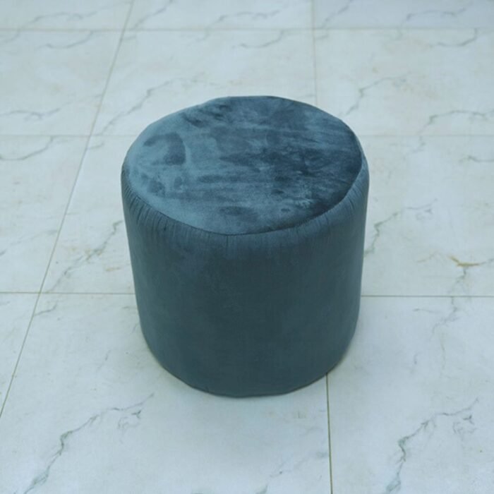 Pouf cylindrique bas en velours bleu orage posé sur un sol clair.