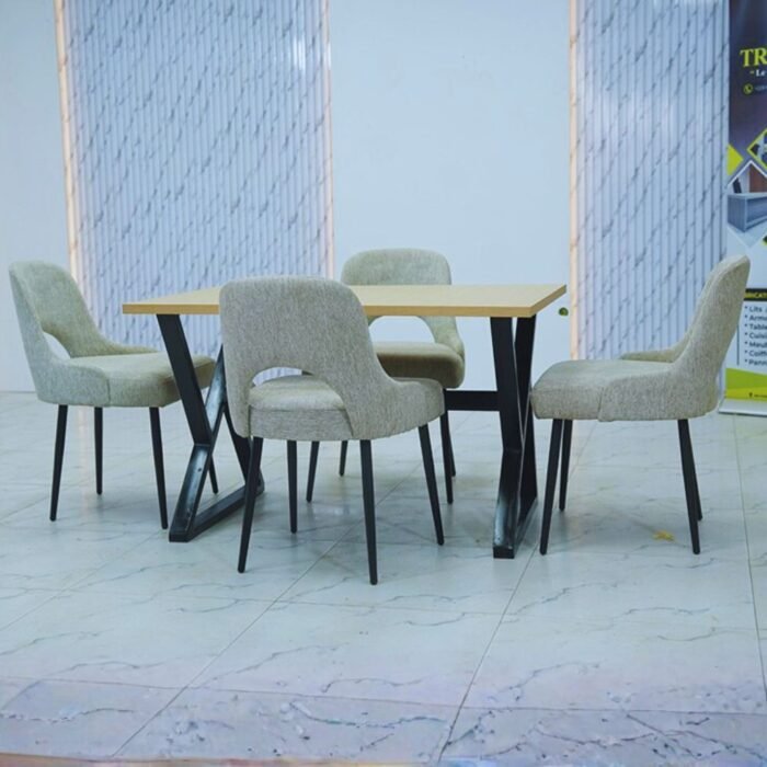 Table à manger en bois clair avec pieds noirs en croix entourée de 4 chaises grises au dossier évidé.