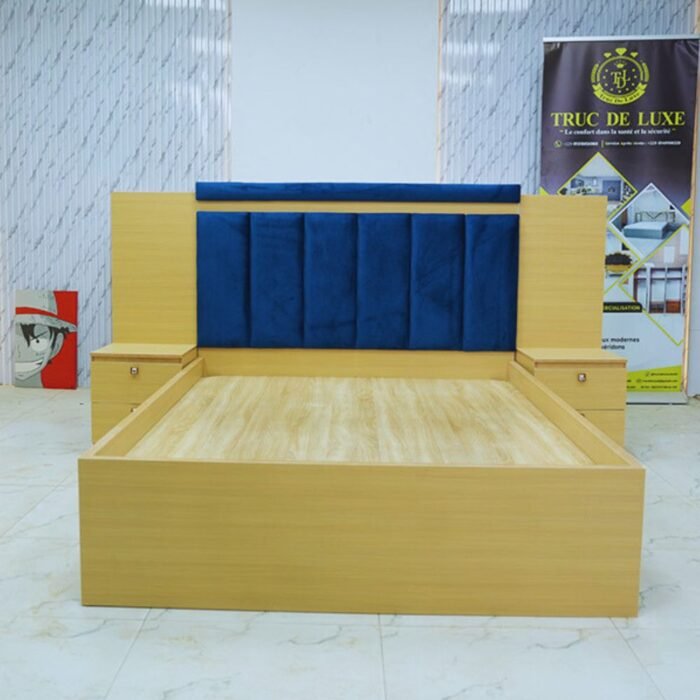 Lit double en bois clair avec tête de lit capitonnée en velours bleu et deux tables de chevet intégrées.