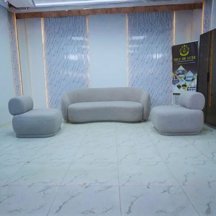 Ensemble de salon gris en tissu bouclé comprenant un canapé incurvé et deux fauteuils ronds sans pieds.
